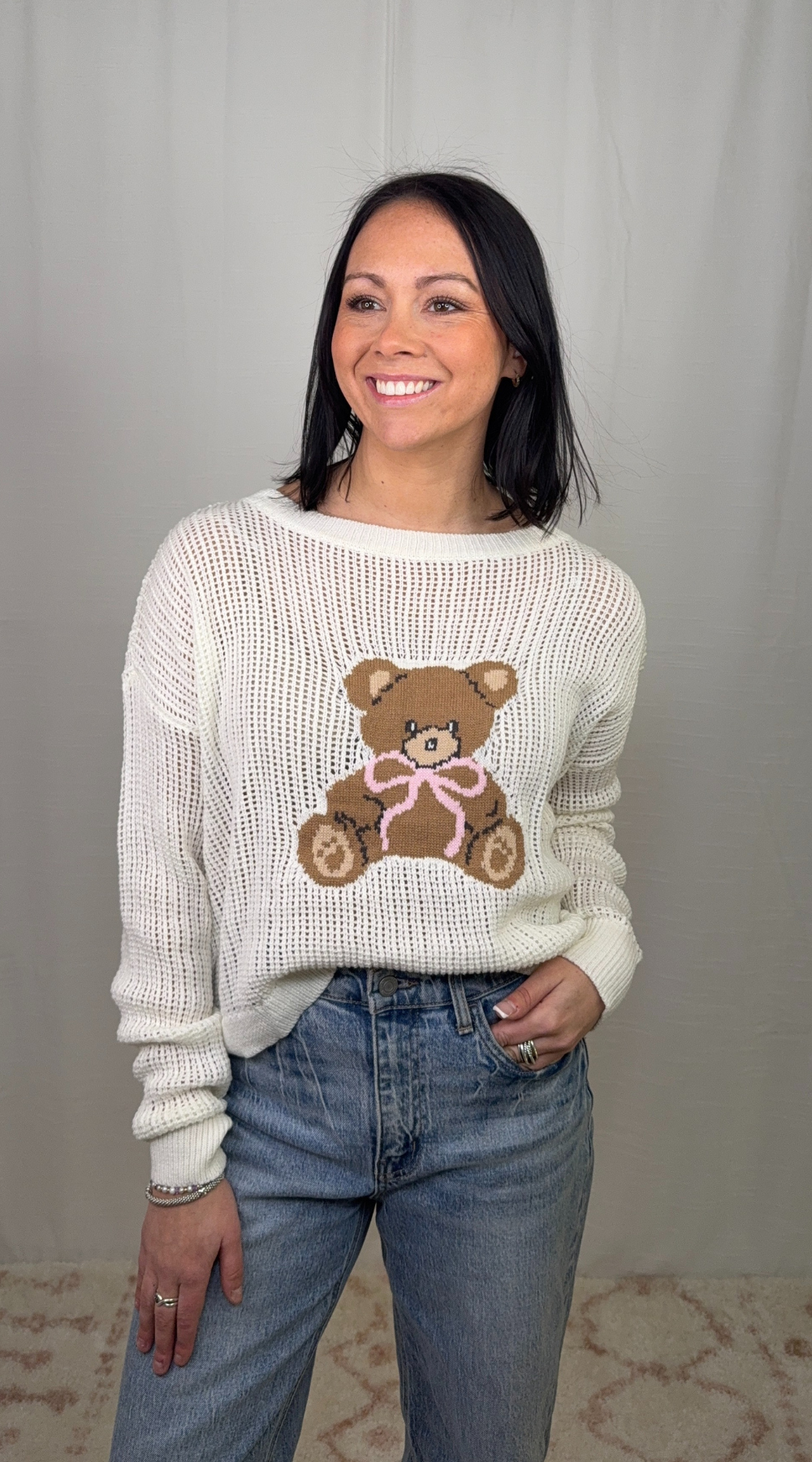 Cream knit sweater with teddy bear graphic worn with blue jeans