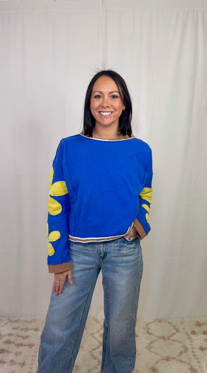 Blue long sleeve top with floral appliqué sleeves worn with blue jeans
