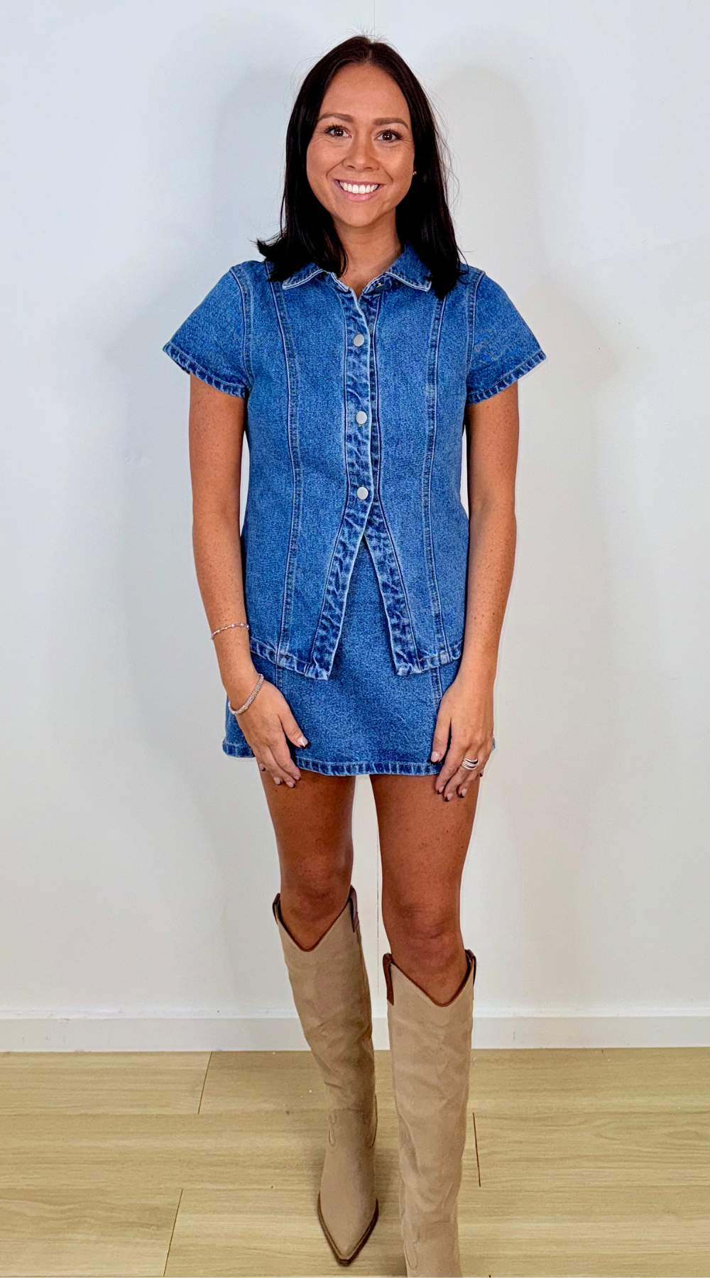 Woman wearing a denim top and skirt with beige knee-high boots on a plain background