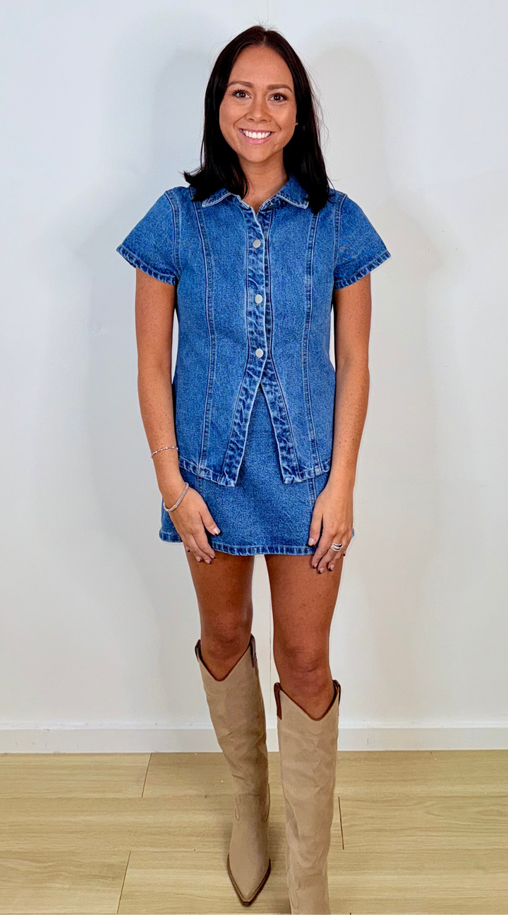 Woman wearing a denim top and skirt with beige knee-high boots on a plain background