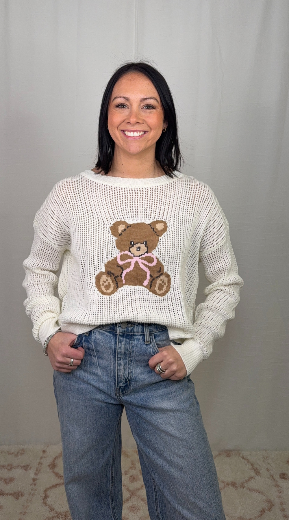 Cream knit sweater with teddy bear graphic worn with blue jeans