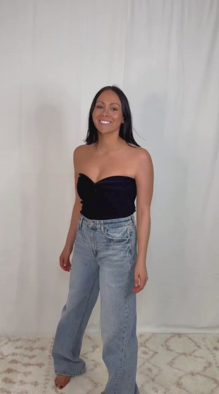 Video of model wearing black strapless twist front top styled with blue jeans